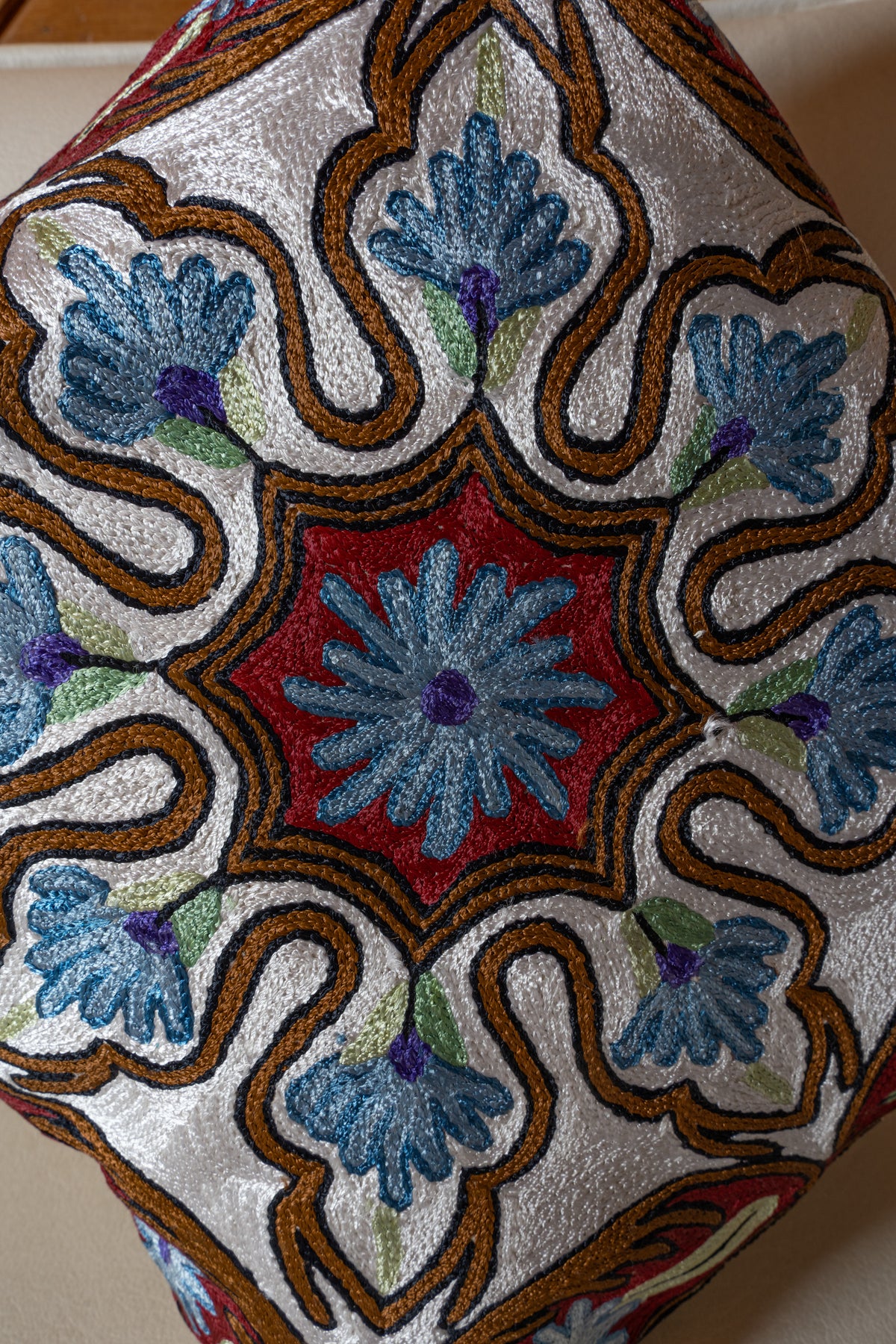 Close-up of blue flower embroidery within ivory petal shapes, outlined in gold and black around a deep red centre
