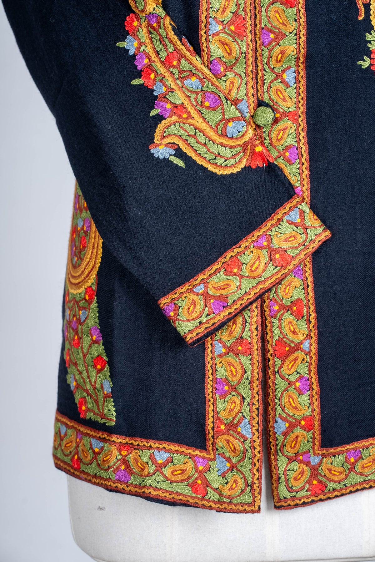 Lower-front detail of the black short jacket, showing colourful Aari borders around the cuff, opening and hem