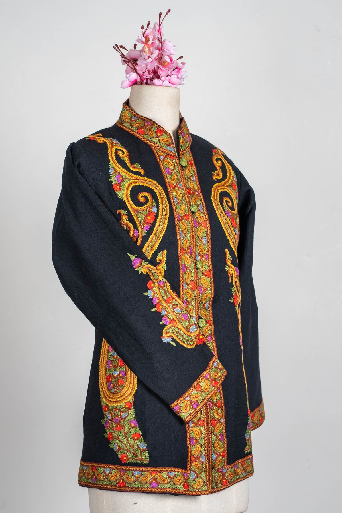 Full angled front view of the black short jacket on a mannequin, with ornate golden-orange scrolls and embroidered collar, cuffs and hem