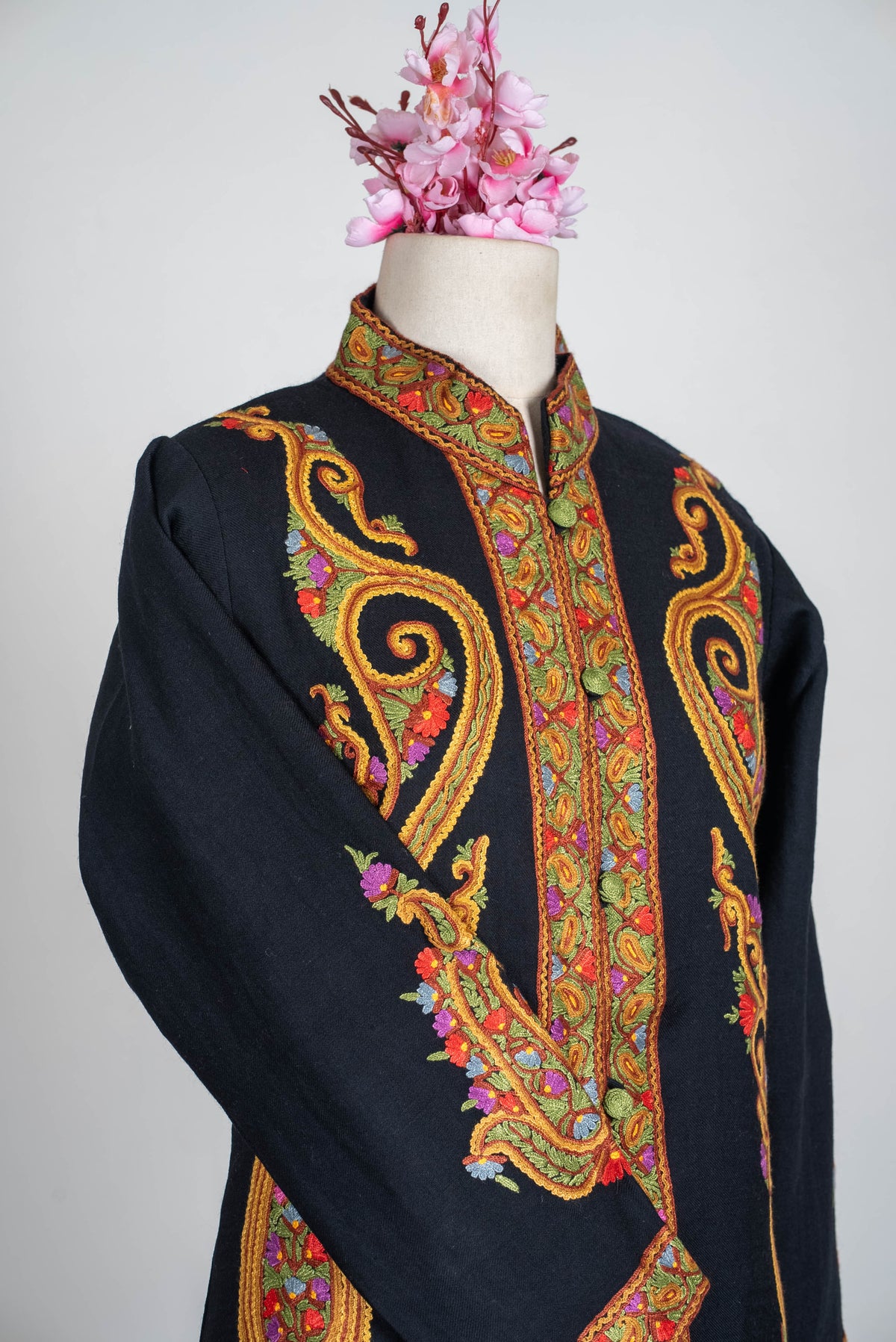 Angled upper-body view of the black short jacket, with golden-orange Aari scrolls framing the buttoned front and crossed sleeve