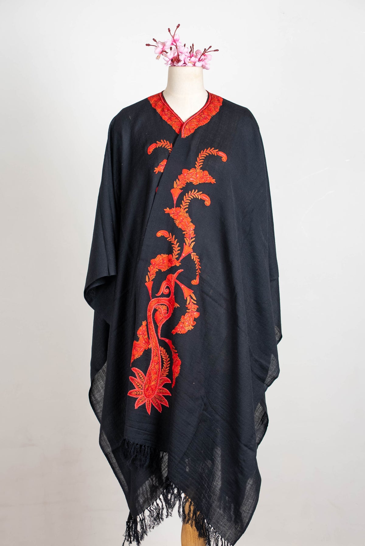 Full-length front view of the black cape on a mannequin, with flowing red-orange paisley embroidery and black fringe