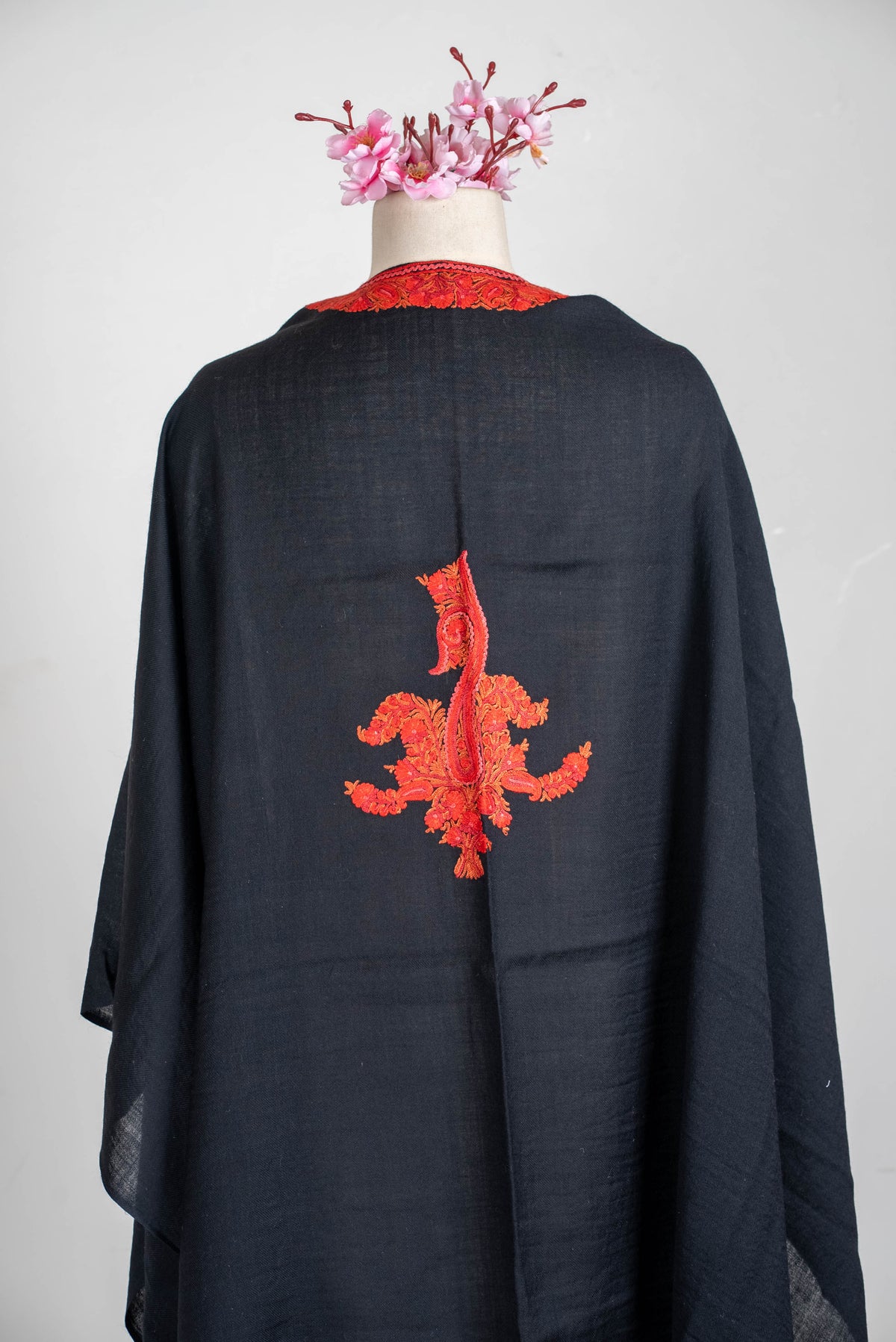 Upper-back view of the black cape, showing red neckline embroidery and a central elongated floral motif