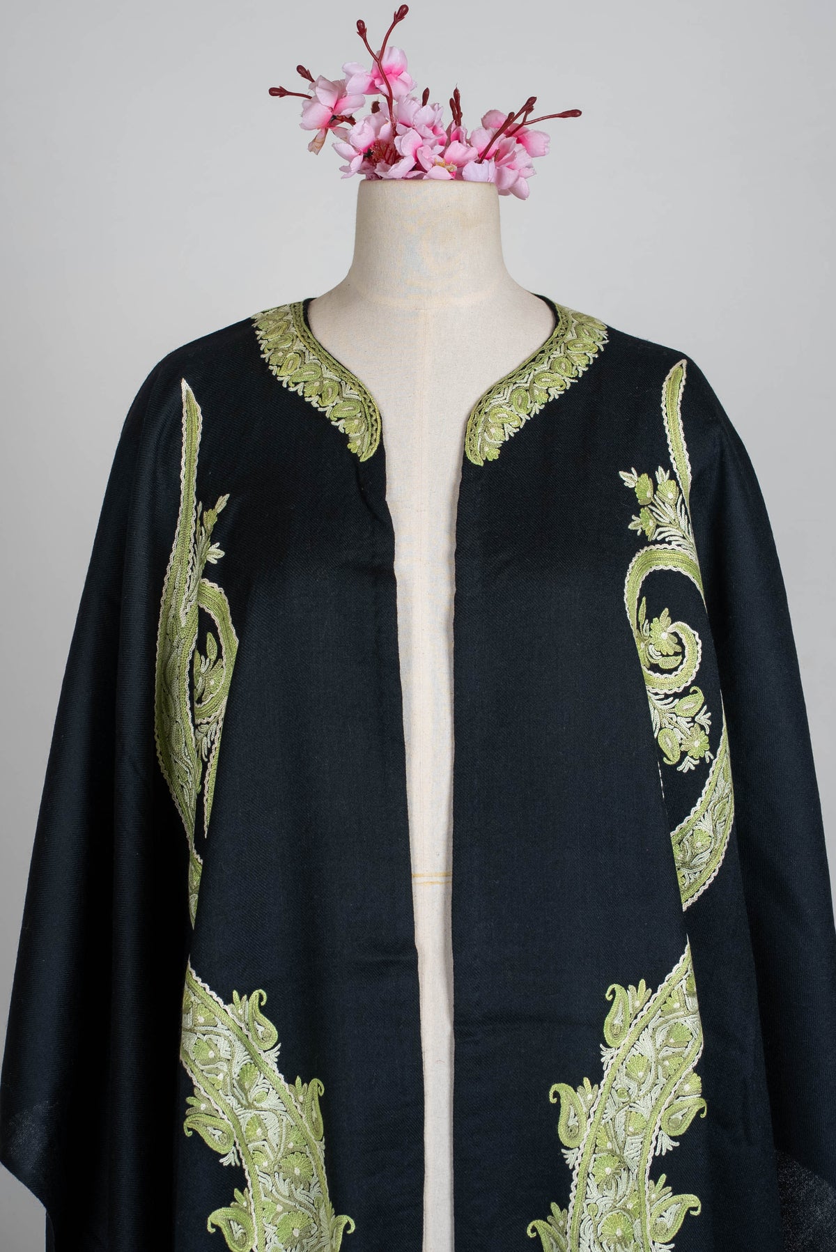 Upper open-front view of the black cape, showing sage-green paisley embroidery on both sides and a decorated neckline