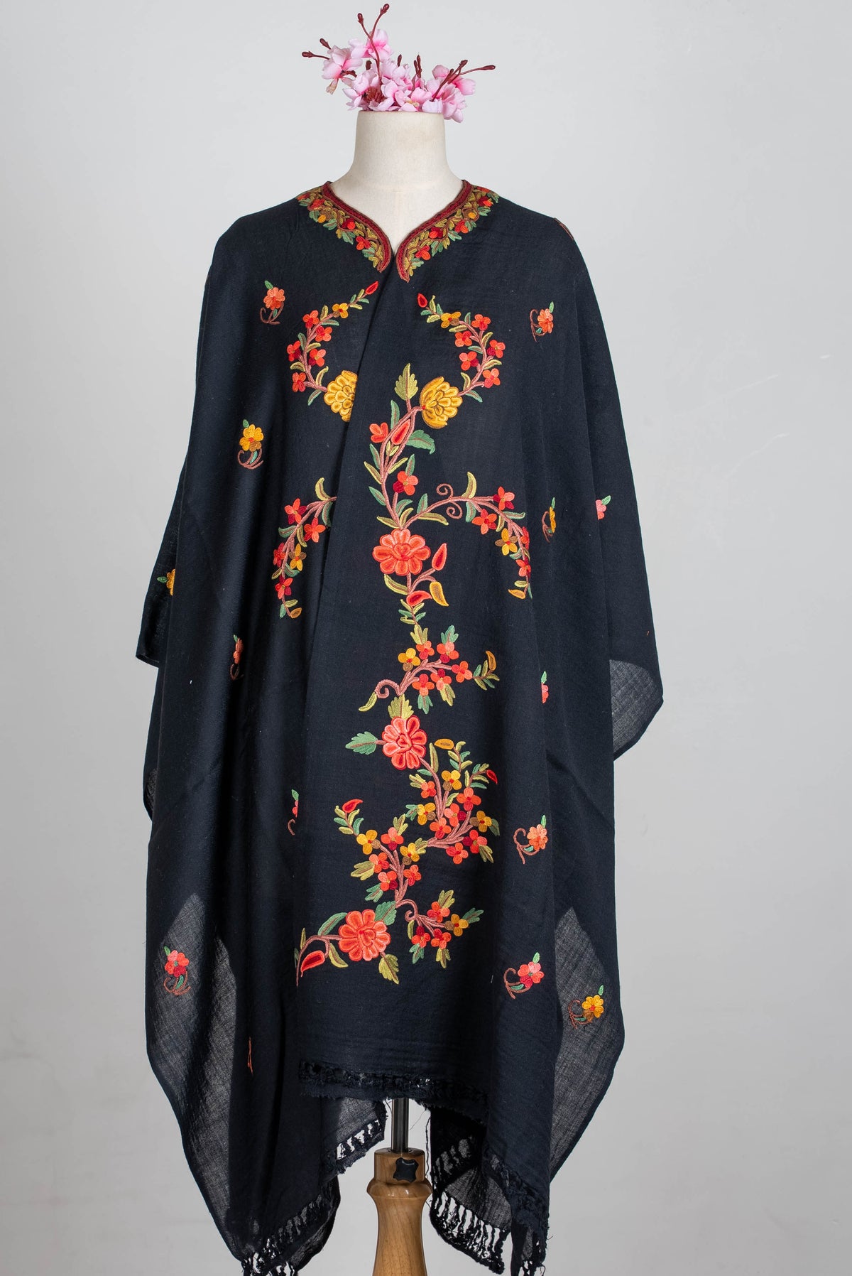 Full front view of the black shawl cape with panels overlapping, showing coral and yellow floral vines and fringed ends