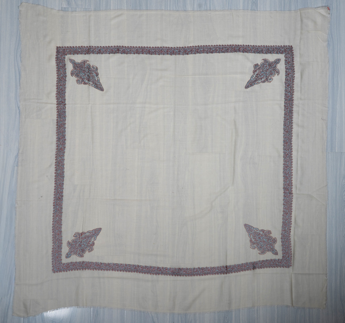 Square ivory Merino wool rumal laid flat with turquoise and coral Sozni borders, four corner motifs and a plain centre