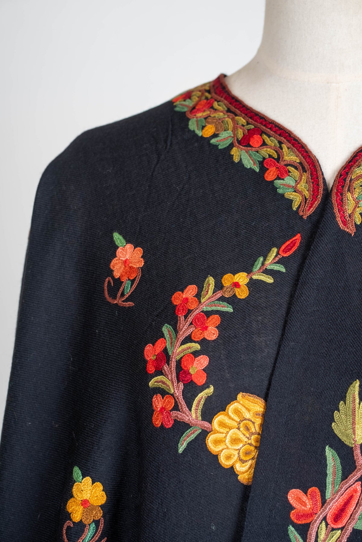 Neckline close-up of the black shawl cape, showing small coral and yellow flowers and green leaves around the curved opening