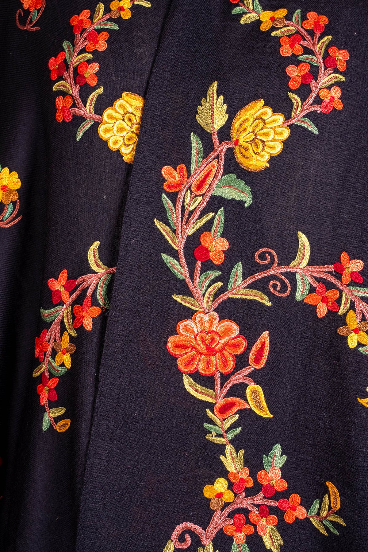 Close-up of coral and yellow embroidered flowers with green leaves and curling stems on the black shawl cape's front