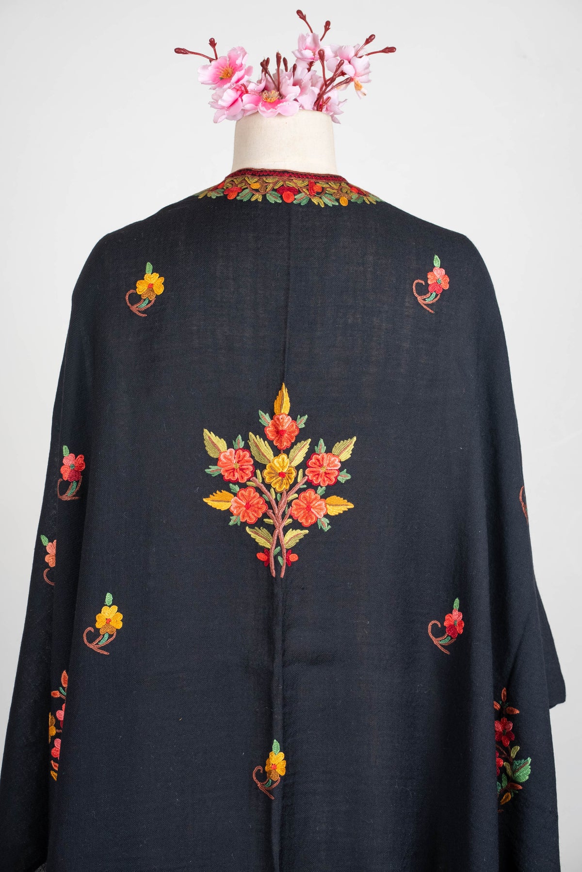 Upper back view of the black shawl cape, showing a central coral and yellow embroidered bouquet and small scattered floral sprigs