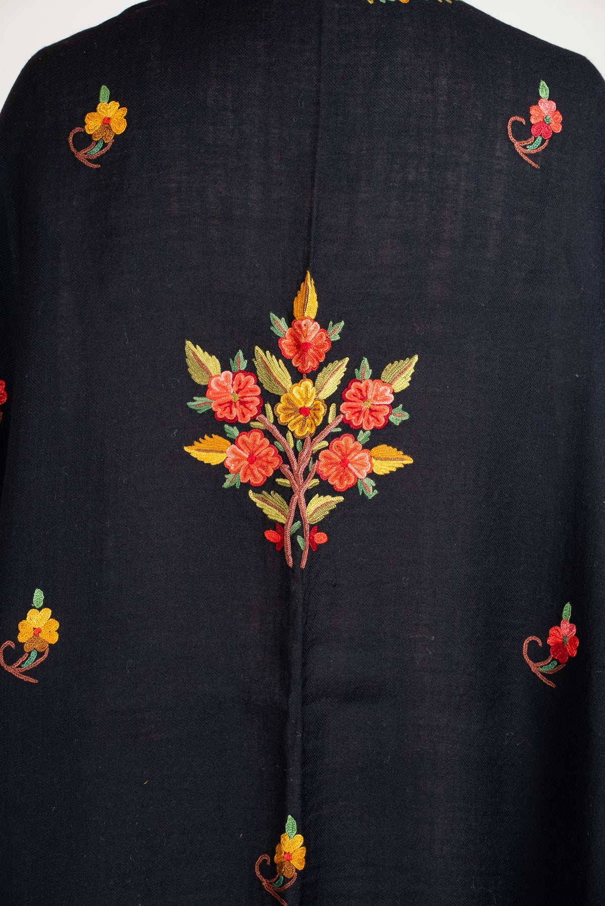 Back close-up of the black shawl cape, with a coral and yellow floral bouquet, green leaves and smaller scattered flowers