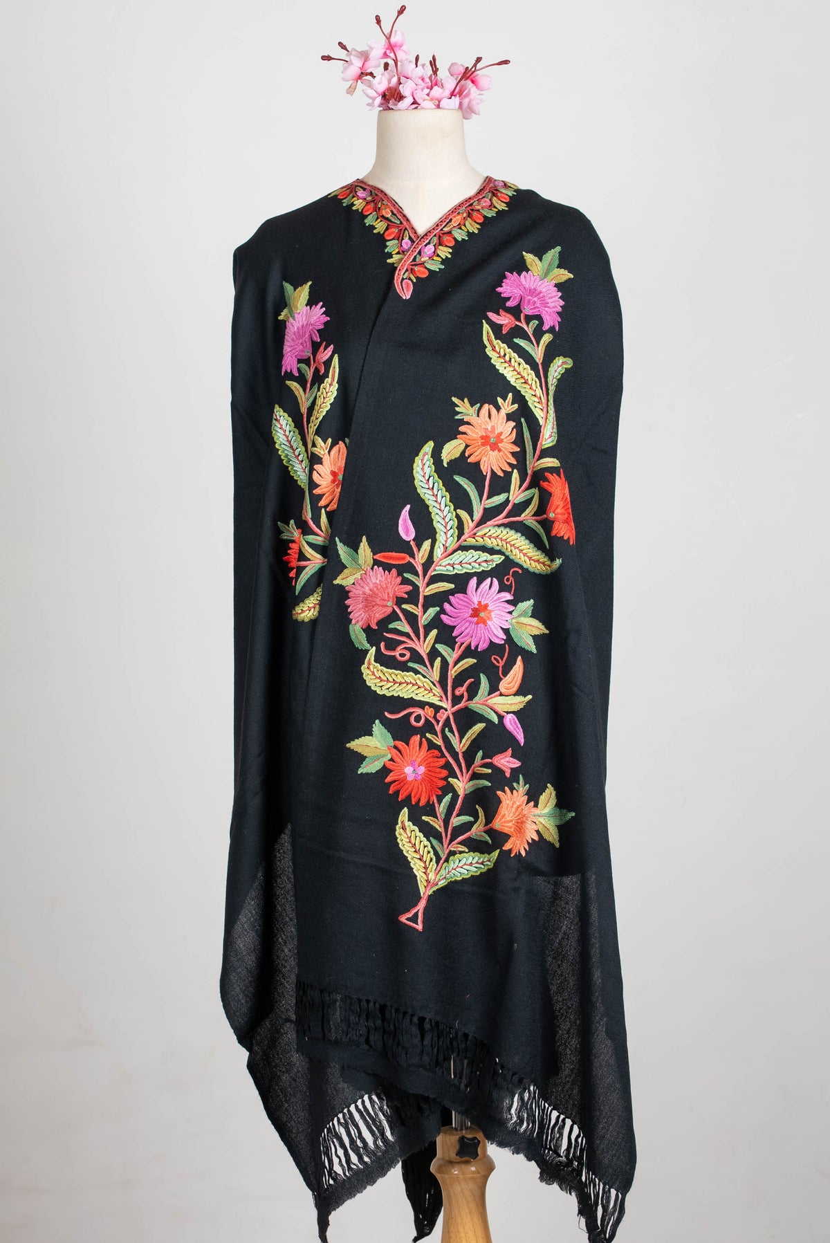 Full front view of the black shawl cape wrapped on a mannequin, with tall pink-and-orange floral stems and black fringe