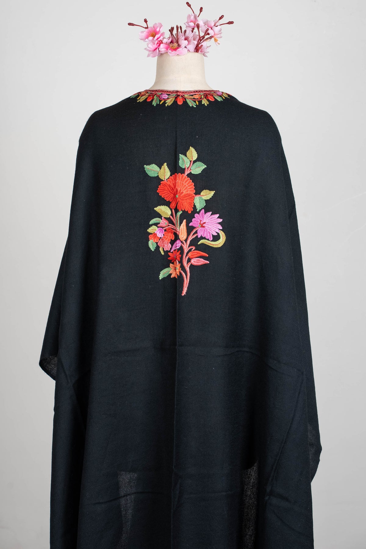Back view of the black shawl cape on a mannequin, with a central red-and-pink floral bouquet below an embroidered neckline