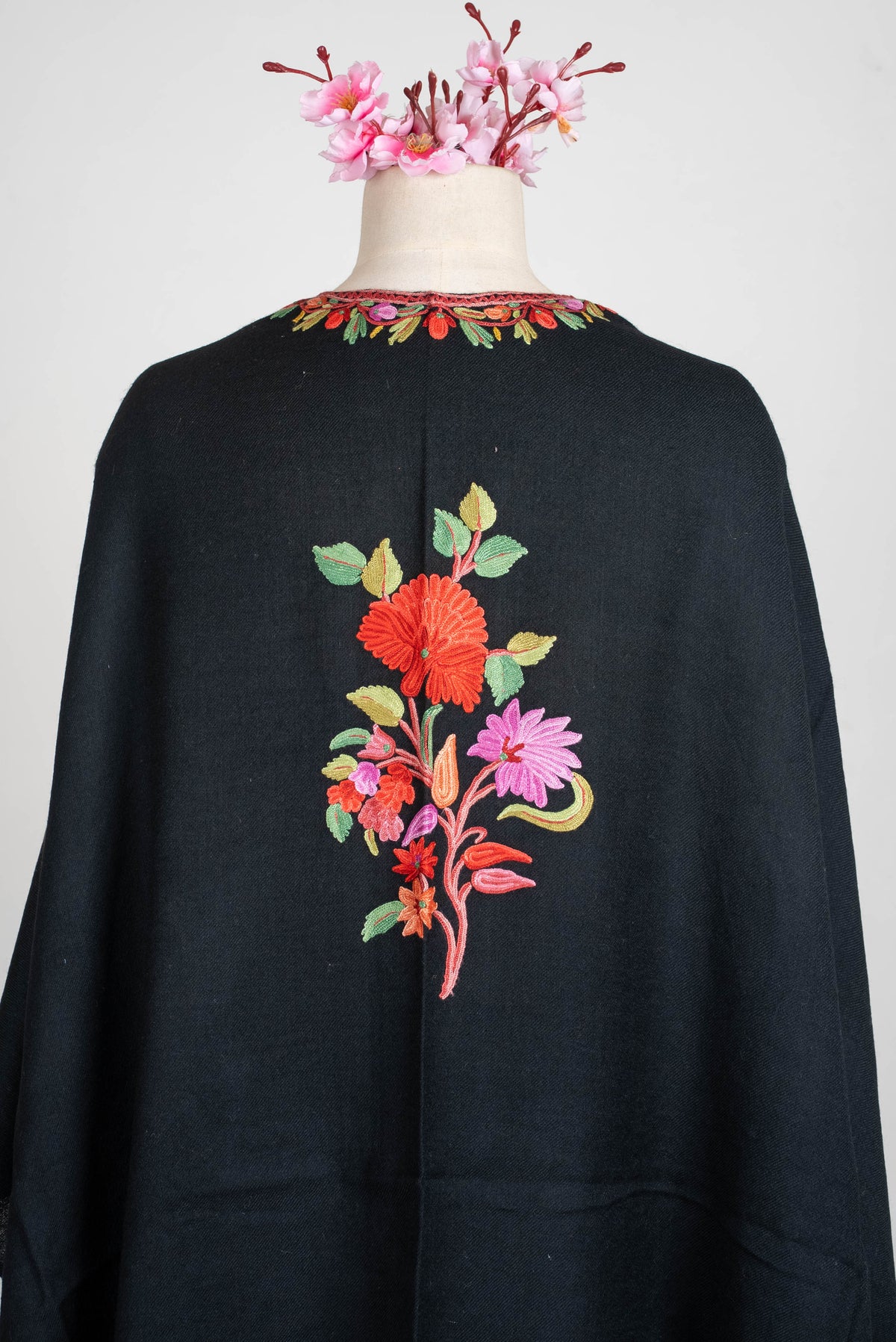 Upper-back detail of the black shawl cape, showing a red flower, smaller pink blossoms and green leaves