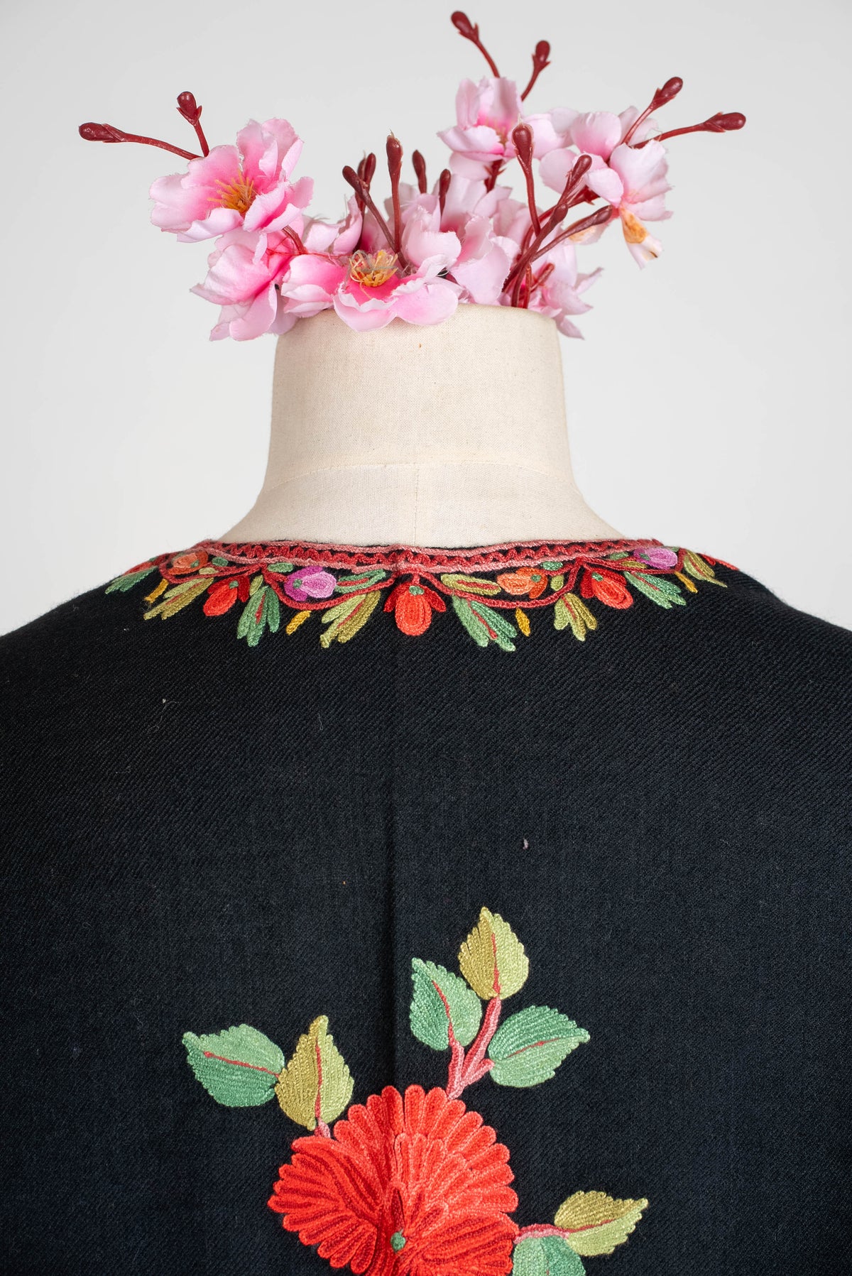 Back-neckline close-up of the black shawl cape, with multicoloured embroidered leaves above a central red flower