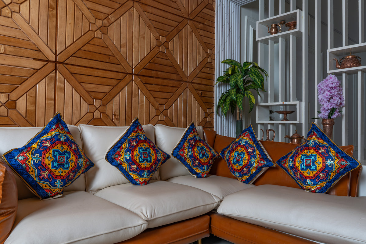 Five matching sapphire blue, red and gold geometric cushions arranged on a cream and tan corner sofa