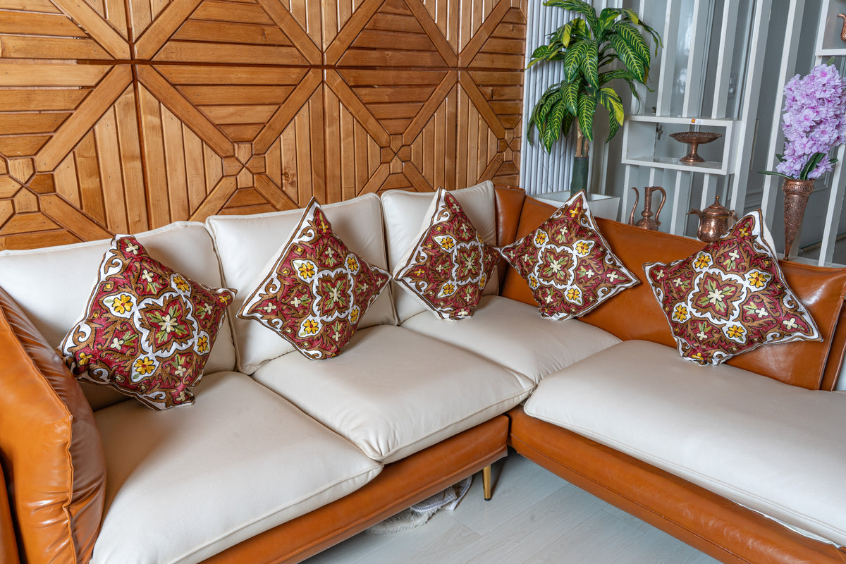 Five matching red, ivory, green and yellow embroidered cushions arranged across a cream corner sofa