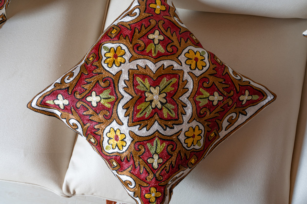 Front view of a cushion with a central green and red floral medallion, ivory outlines and yellow flowers