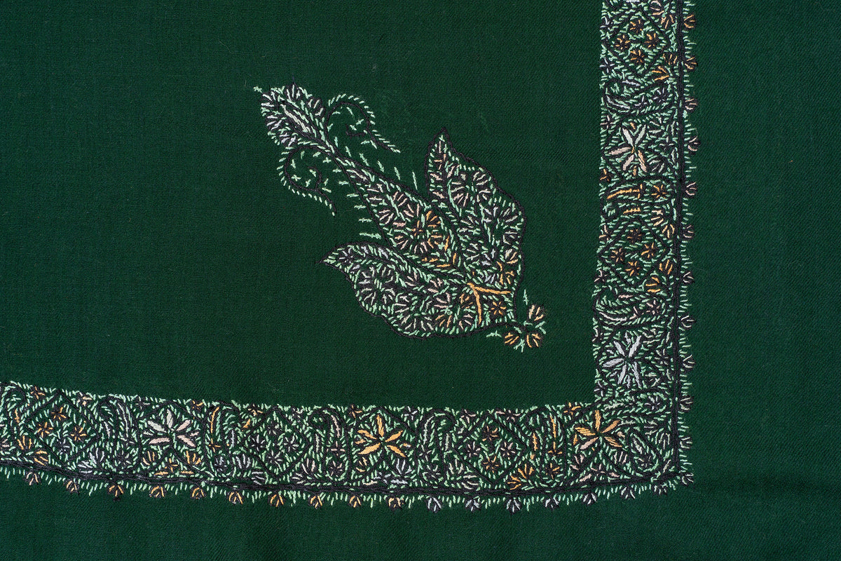 Flat corner detail of a dark green rumal with a pale floral border, ochre accents and a separate paisley motif