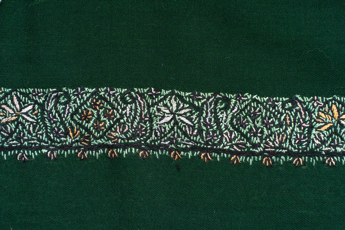 Close-up of pale floral stitches and small ochre flowers along the border of a dark green rumal