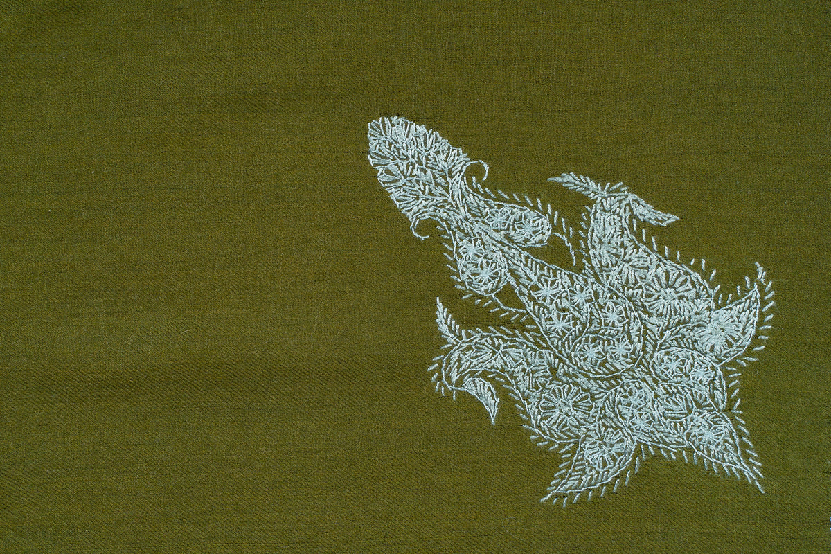 Close-up of a pale blue Sozni paisley densely filled with small leaf stitches on olive-green fabric