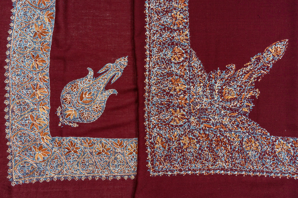 Folded crimson rumal revealing the front and reverse of multicoloured Sozni corner motifs and broad floral borders