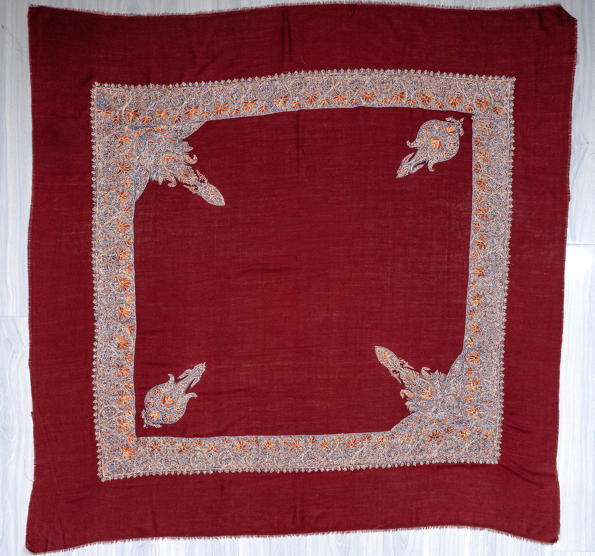 Square crimson Merino wool rumal laid flat with multicoloured Sozni borders, four corner motifs and a plain centre
