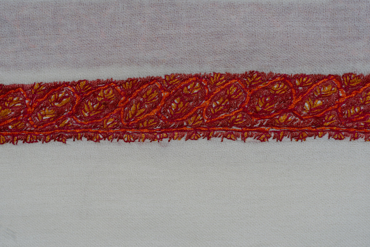 Close-up of red-orange Sozni flowers and curling leaves along an ivory rumal border