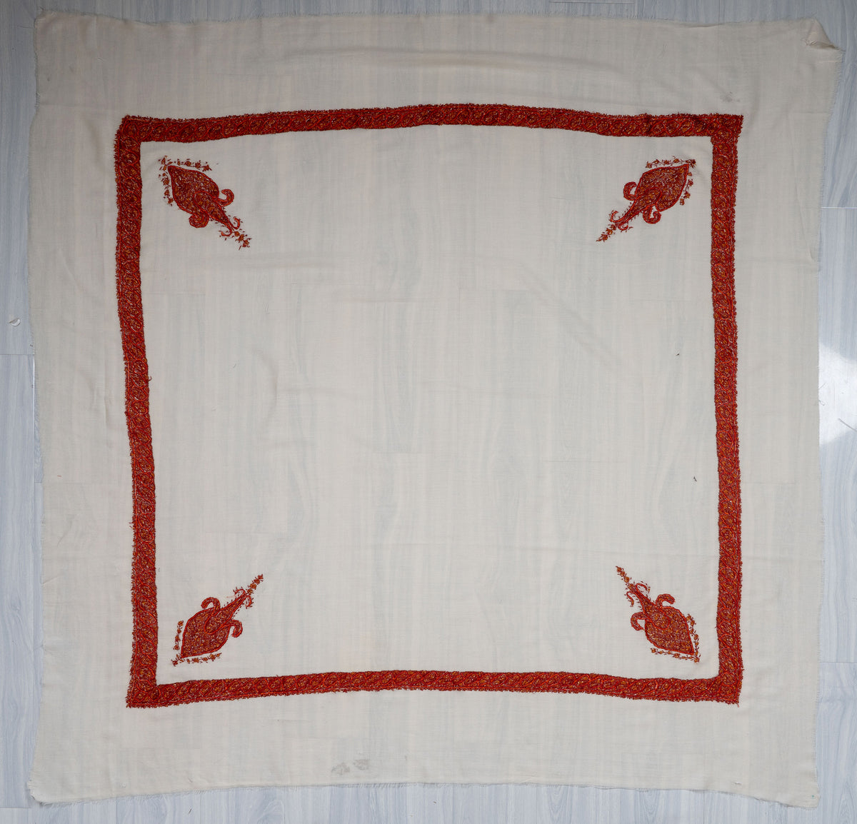 Square ivory Merino wool rumal laid flat with red-orange Sozni borders, four corner motifs and a plain centre