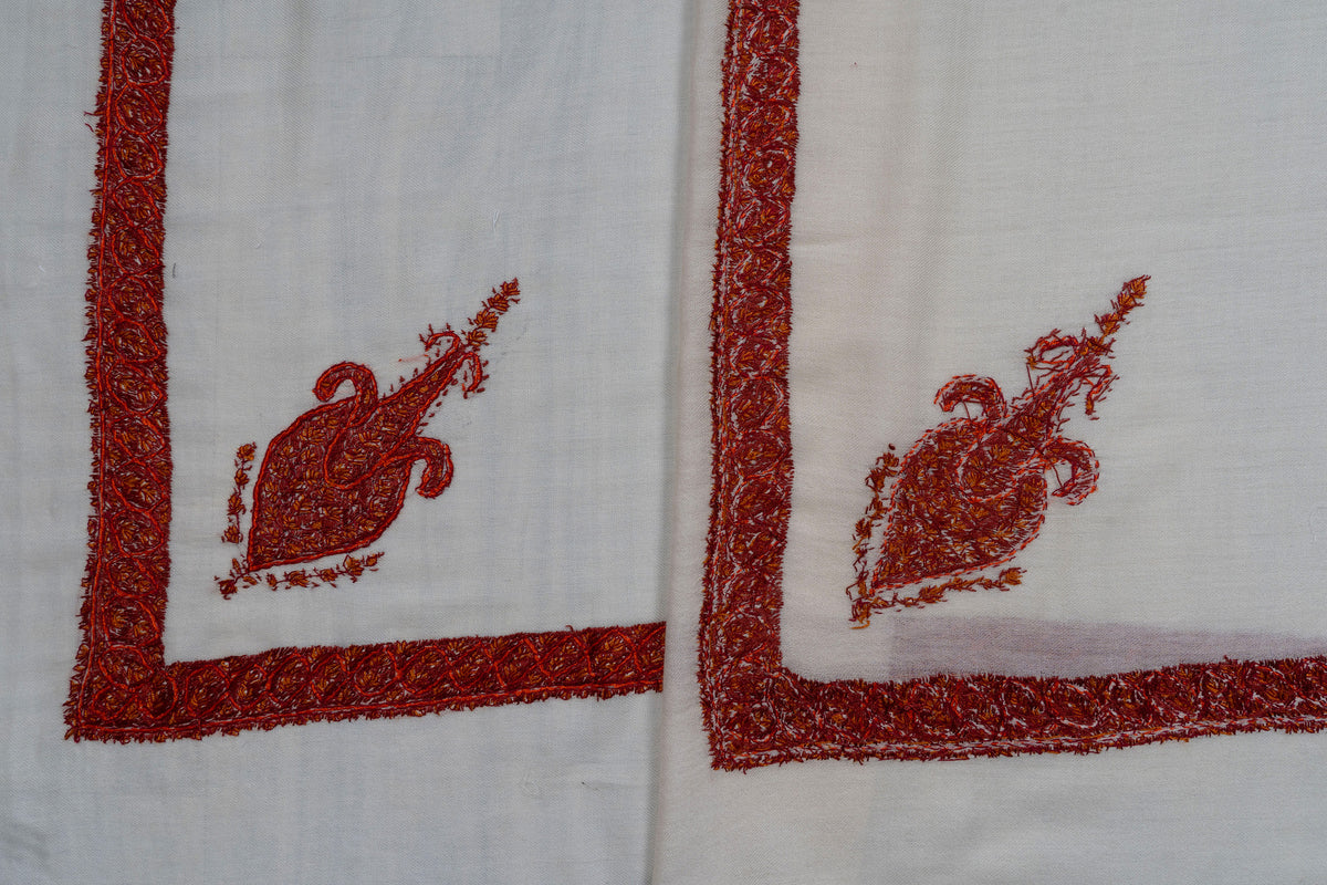 Overlapping ivory rumal corners showing both sides of red-orange Sozni motif and border stitching