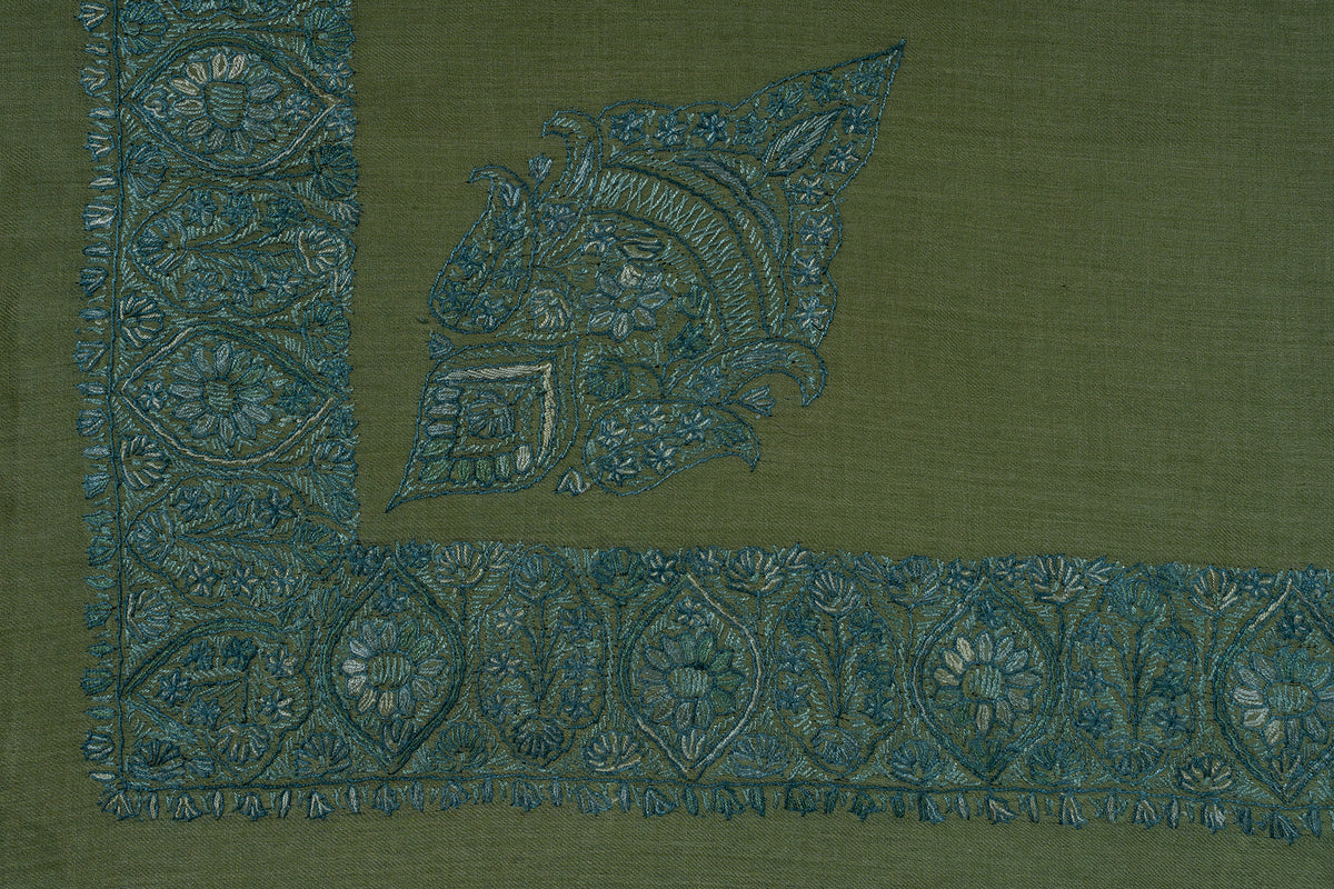 Flat corner of the olive rumal showing a teal leaf-shaped motif beside a broad embroidered floral border