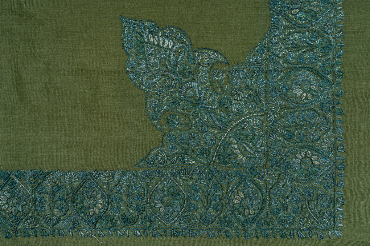 Corner detail of the olive rumal with a large teal floral motif joining the embroidered border