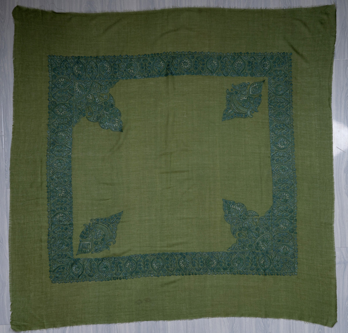 Square olive-green Merino wool rumal spread flat, with a plain centre, broad teal border and four corner motifs