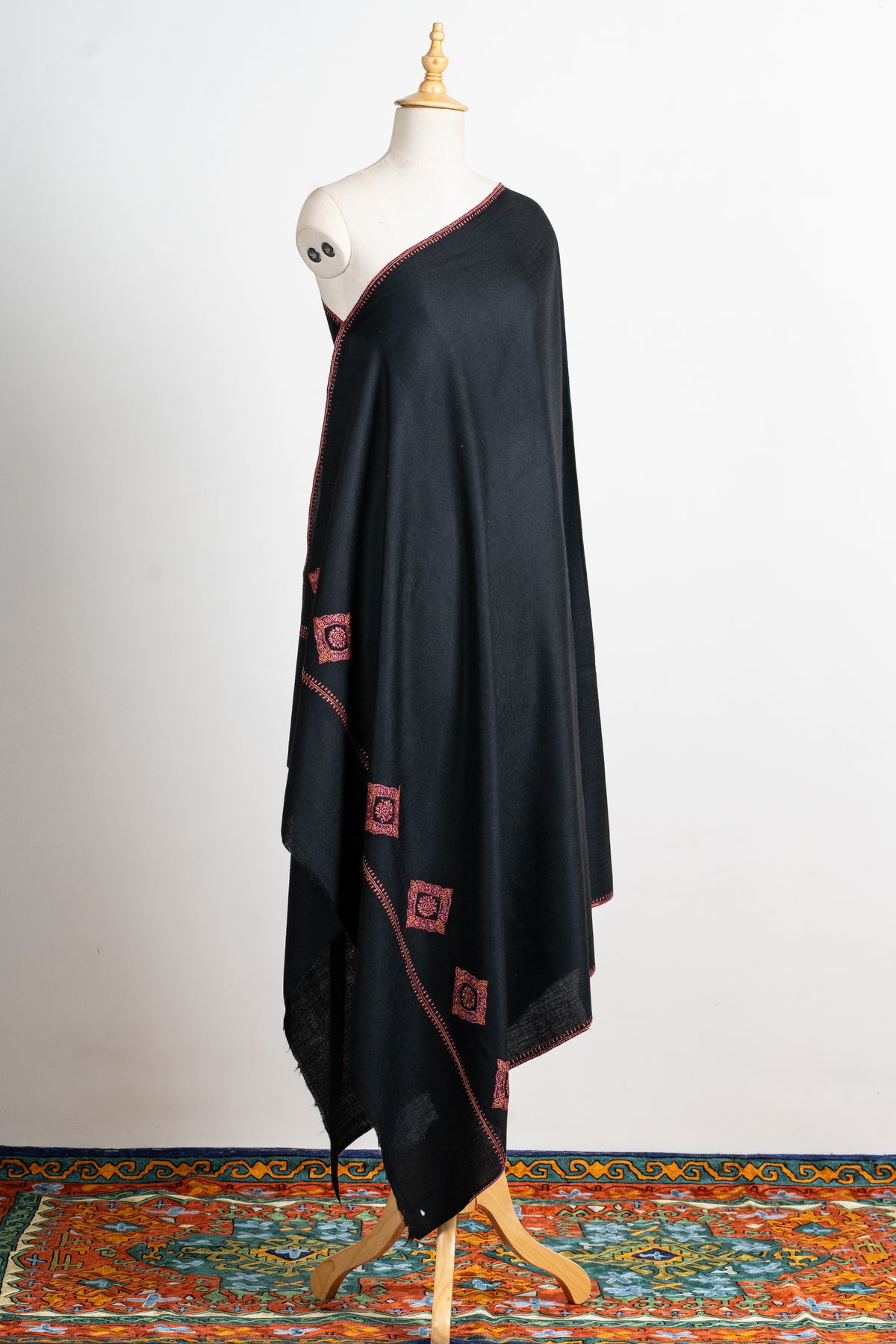 Full draped view of the black shawl on a mannequin, with red diamond-shaped motifs near the end and narrow edging.