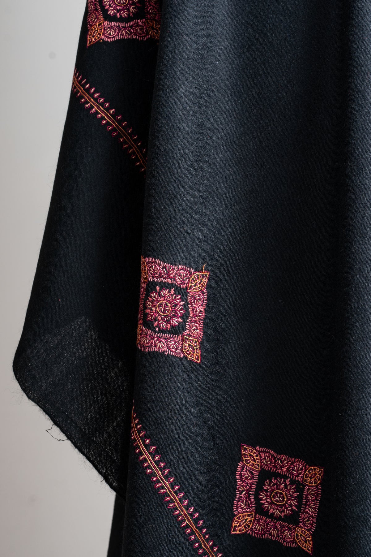 Hanging black shawl end with red diamond-shaped floral motifs above a narrow embroidered band.