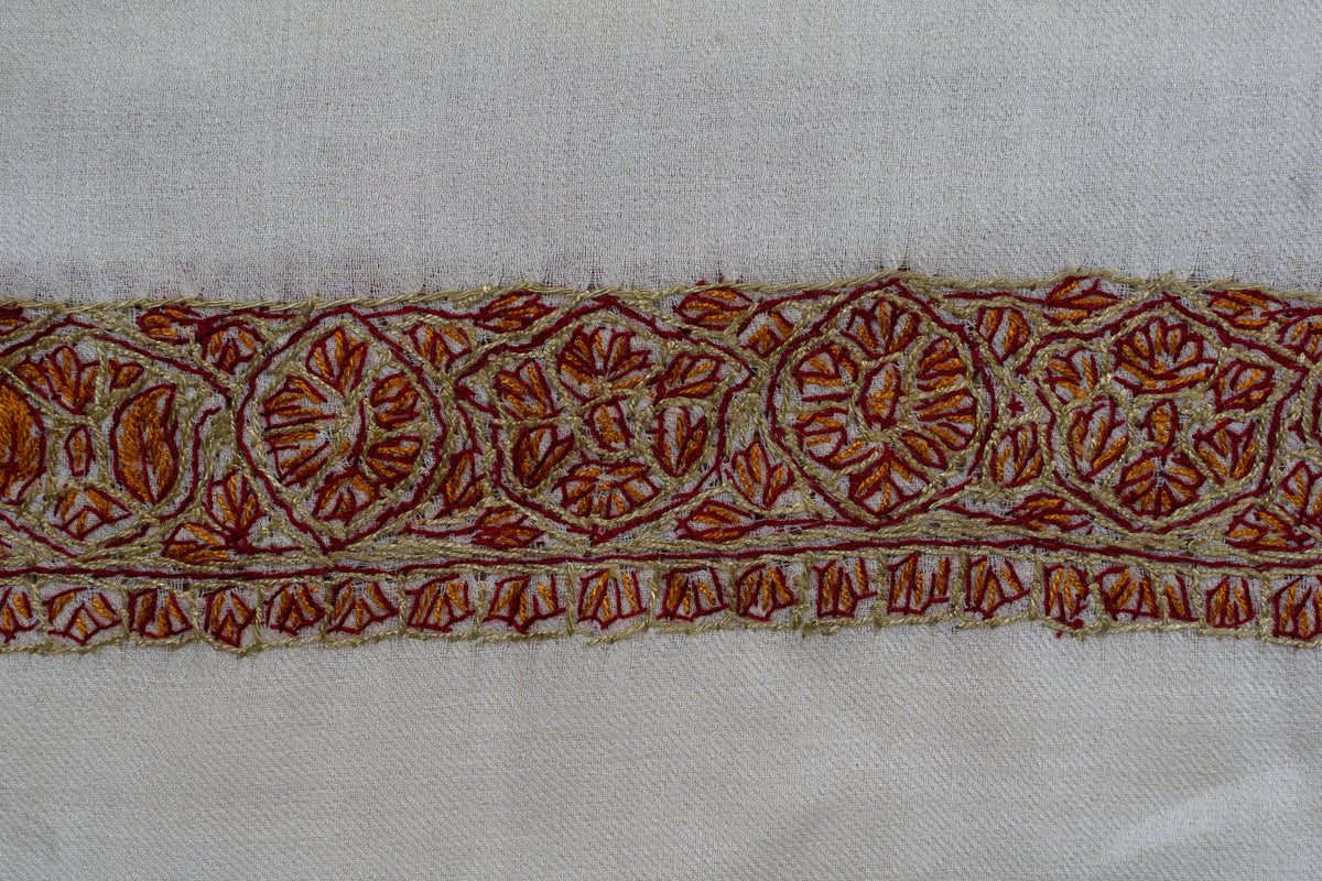 Close-up of rust and gold Sozni flowers inside rounded border panels on ivory fabric