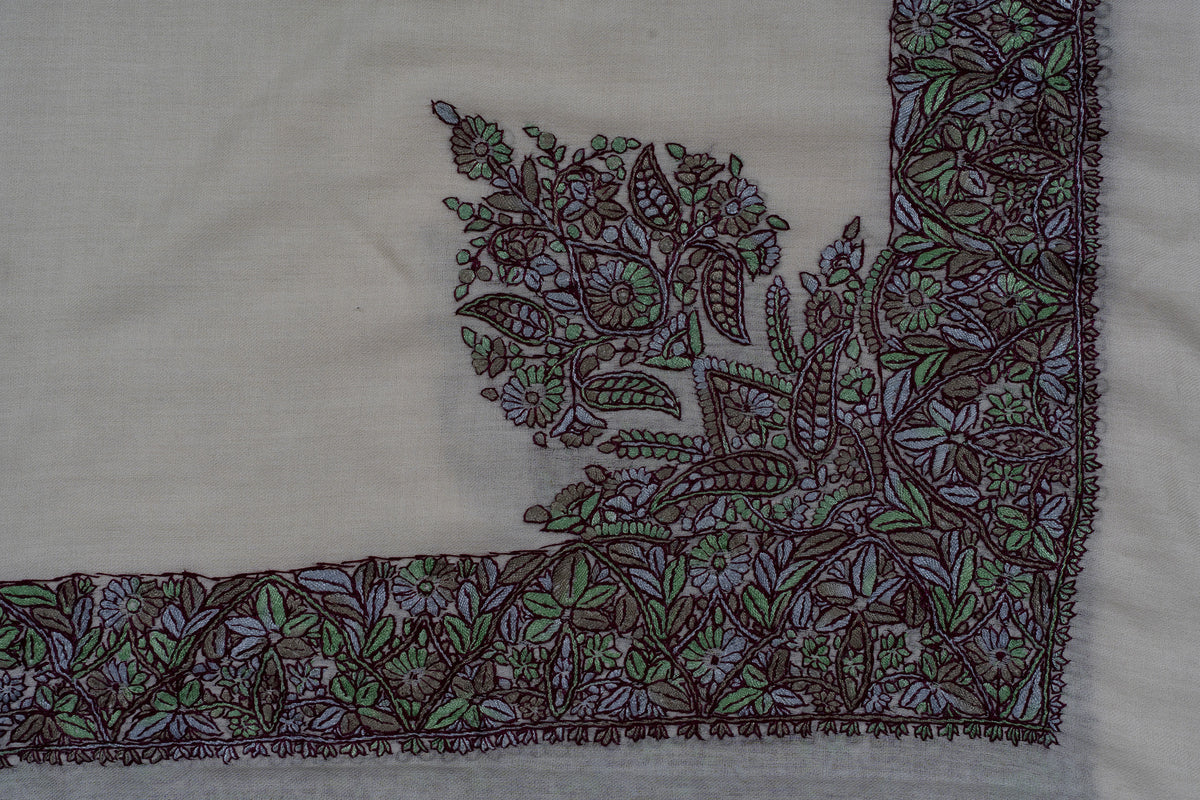 Corner of an ivory rumal with purple and green floral embroidery extending inward from a broad leafy border