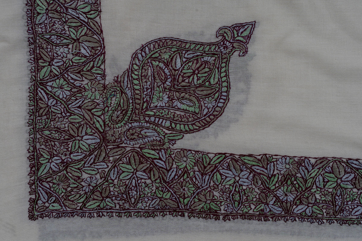 Flat corner detail of an ivory rumal with a large pointed floral motif joined to purple-and-green embroidered borders