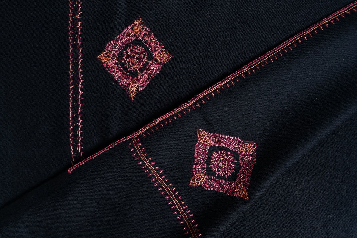 Overlapping black shawl ends showing red floral medallions, narrow edging and the reverse of the embroidery.
