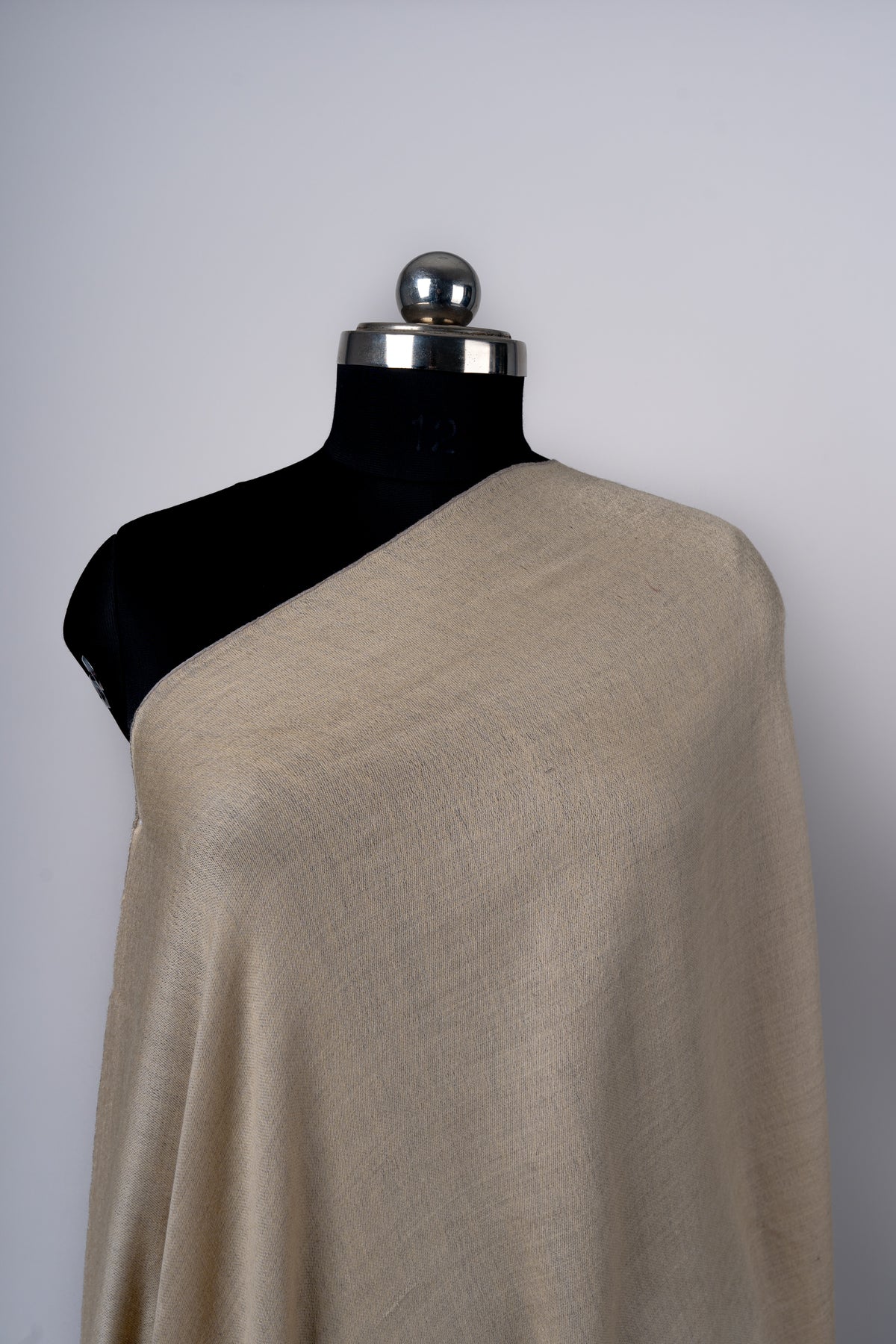 Close-up of the beige side of a reversible Merino wool stole across a mannequin’s shoulder, showing its fine woven texture