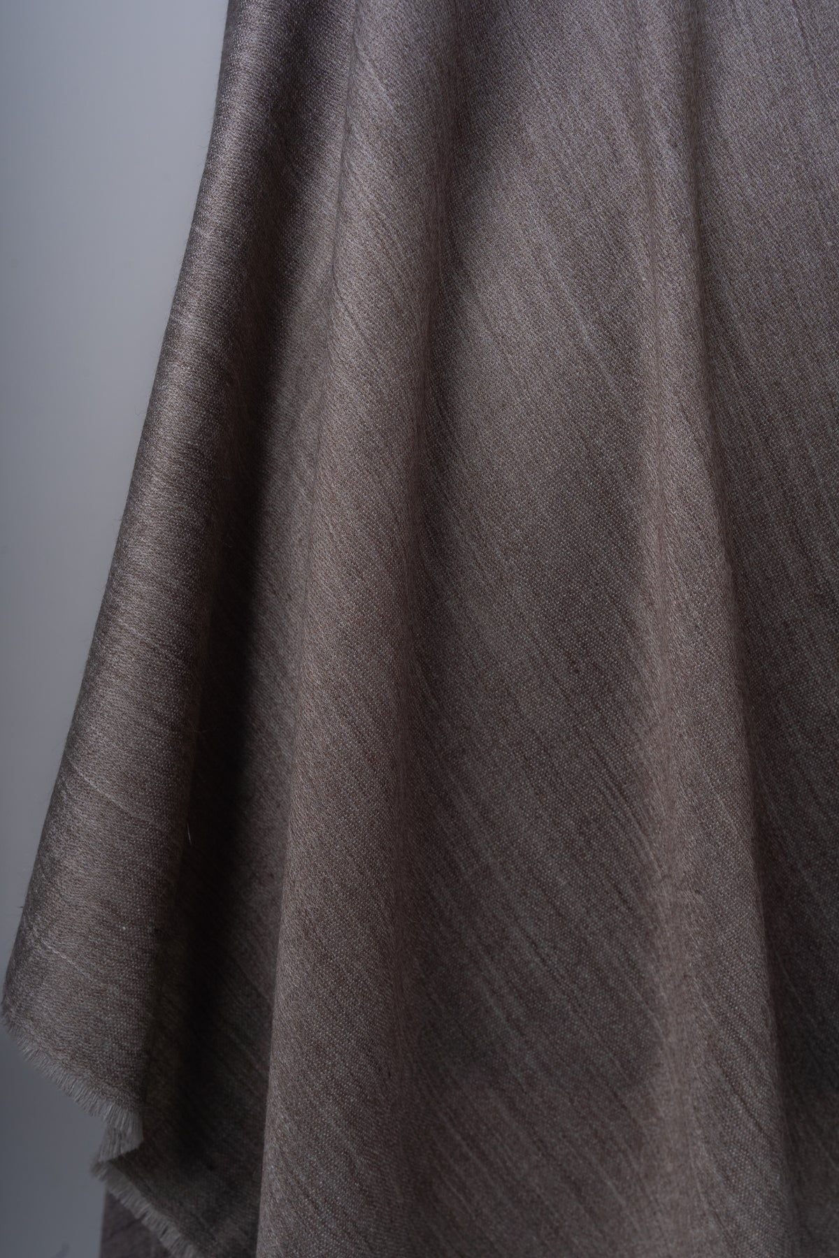 Detail of the hanging mocha stole with soft folds, fine woven texture and a lightly fringed edge.