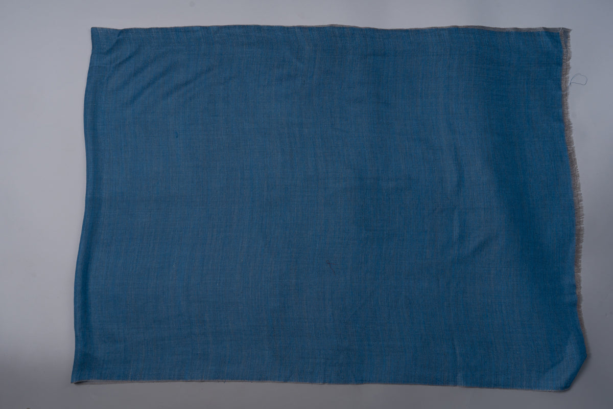 Azure-blue side of the reversible merino wool stole laid flat, showing the plain field and fine fringed edge.