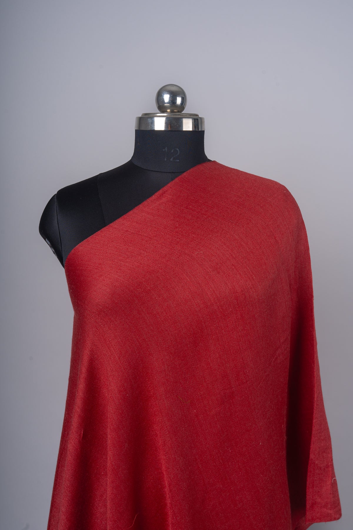 Close-up of the crimson stole across a mannequin’s shoulder, showing the plain woven fabric and diagonal edge