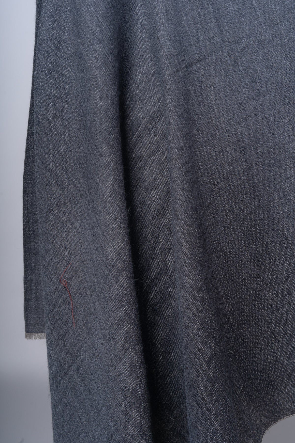 Detail of the hanging charcoal fabric with soft folds, a fine weave and a lightly fringed lower edge.