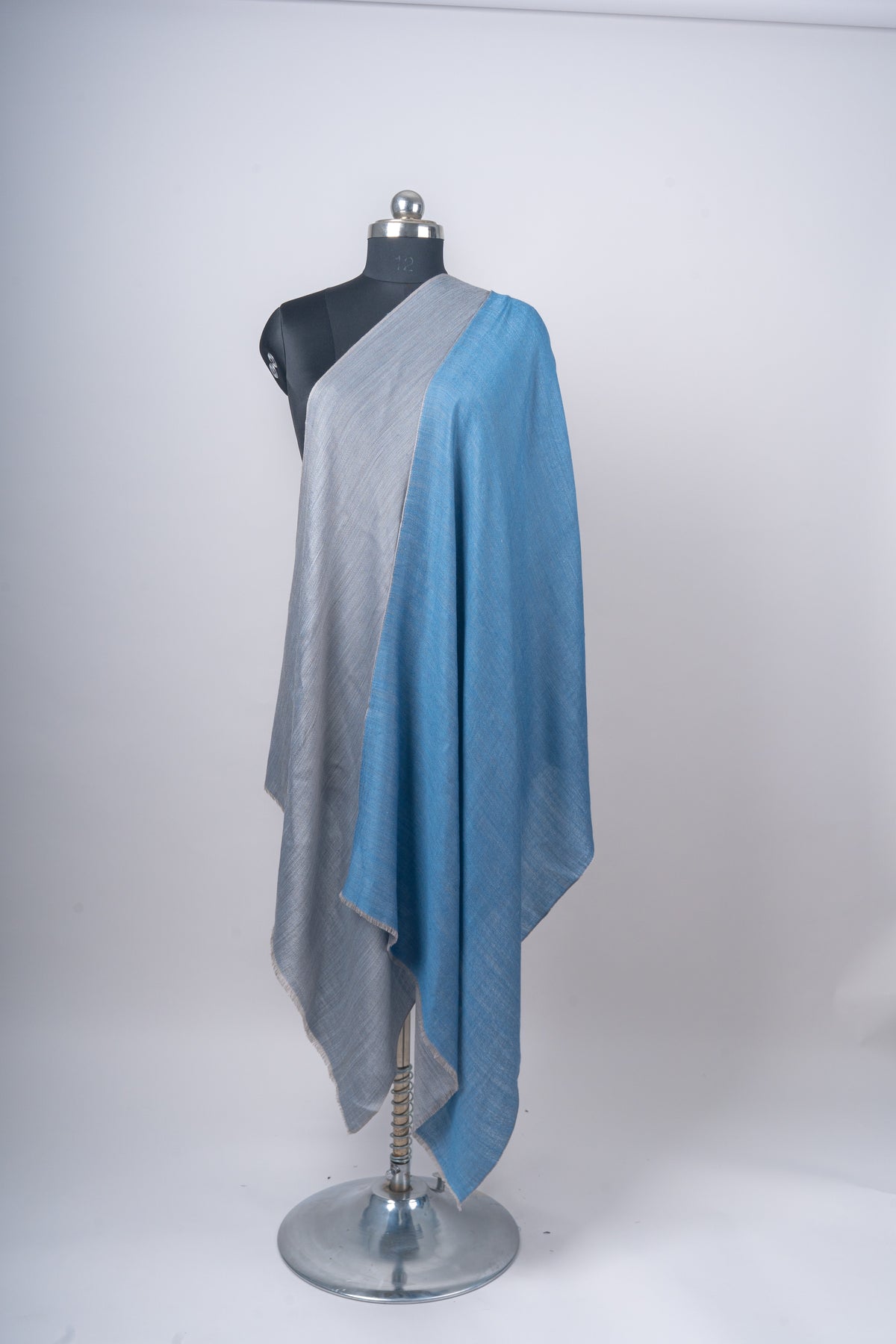 Reversible stole draped on a mannequin with the steel-grey side folded outward beside the azure-blue side.