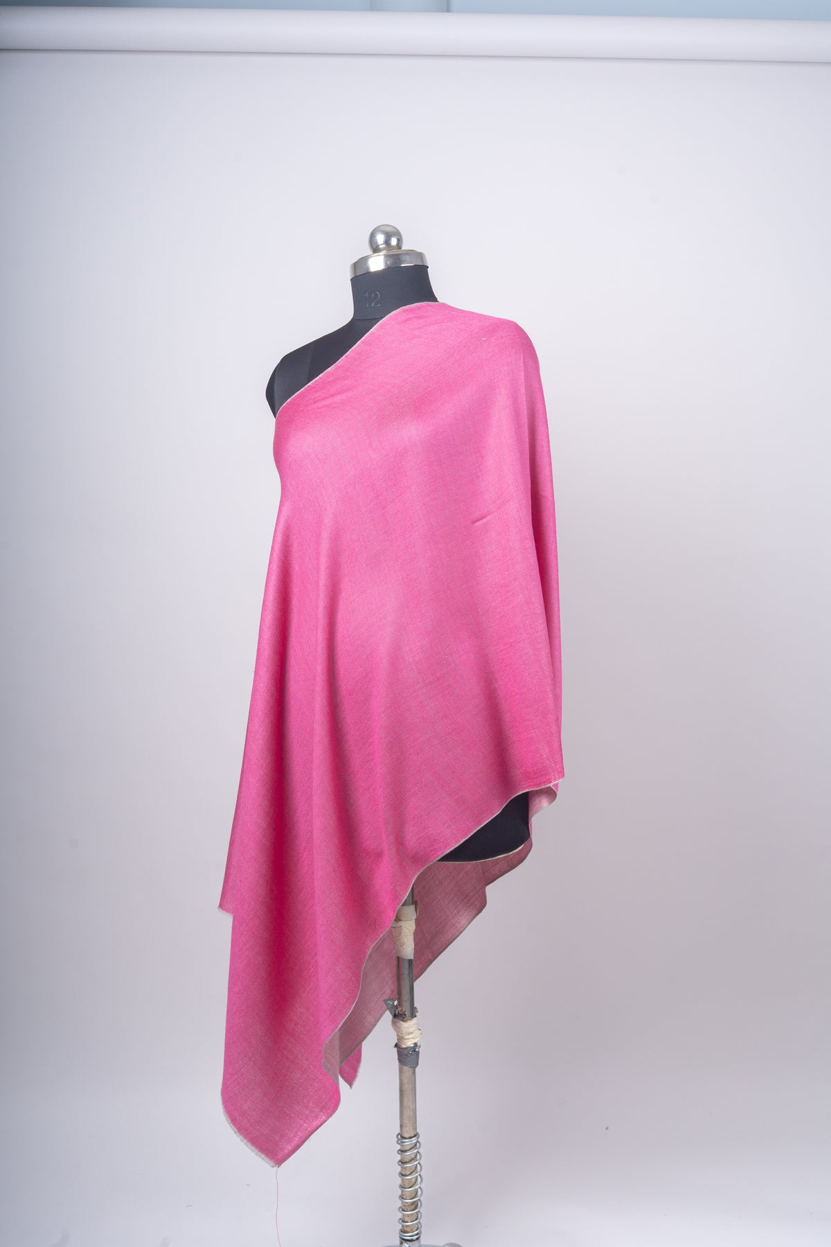 Angled full view of a pink reversible stole on a black mannequin, with a pale rose underside visible along the hanging edge