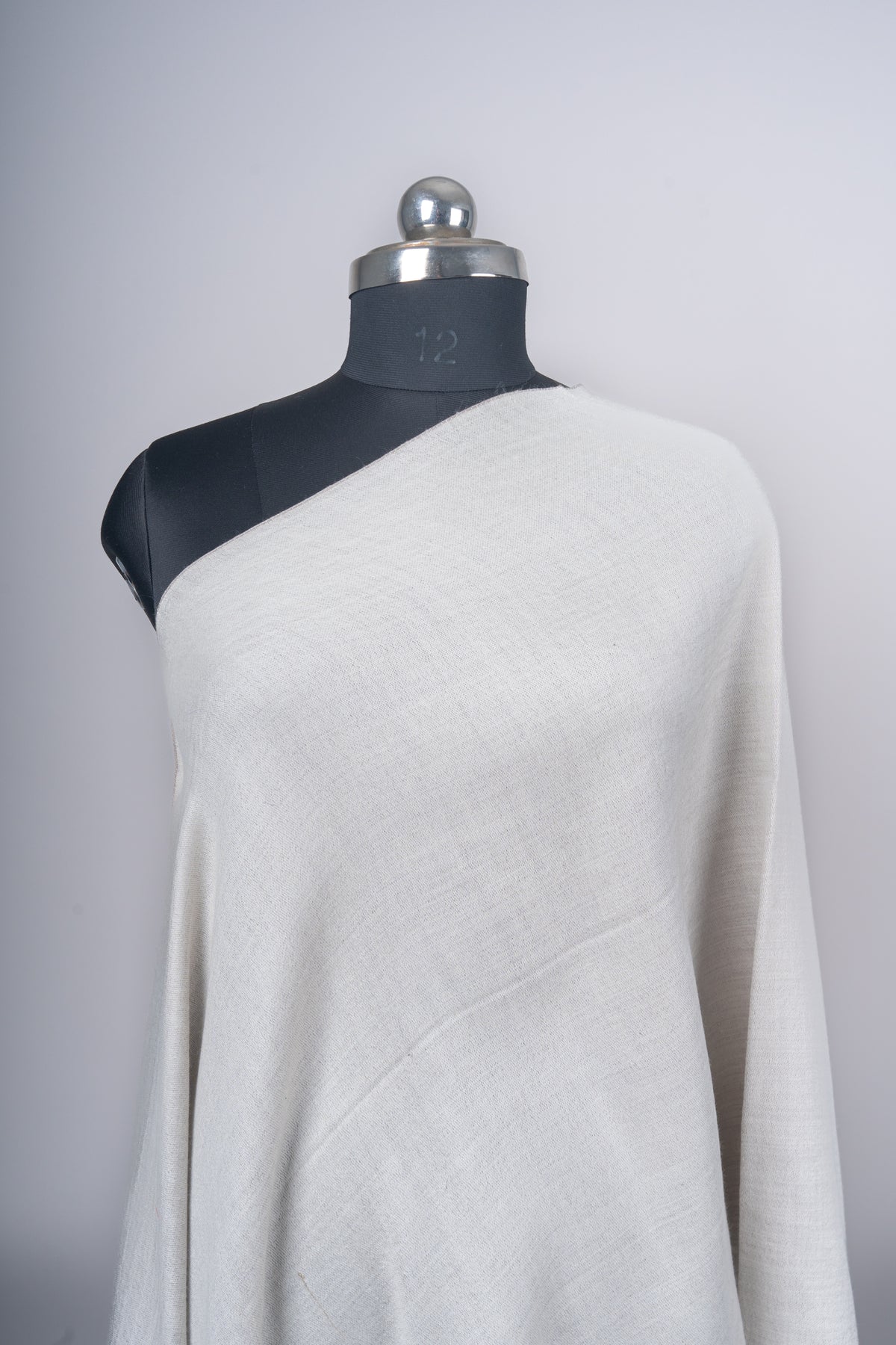 Close view of the plain ivory side of the Merino wool stole draped diagonally across a mannequin