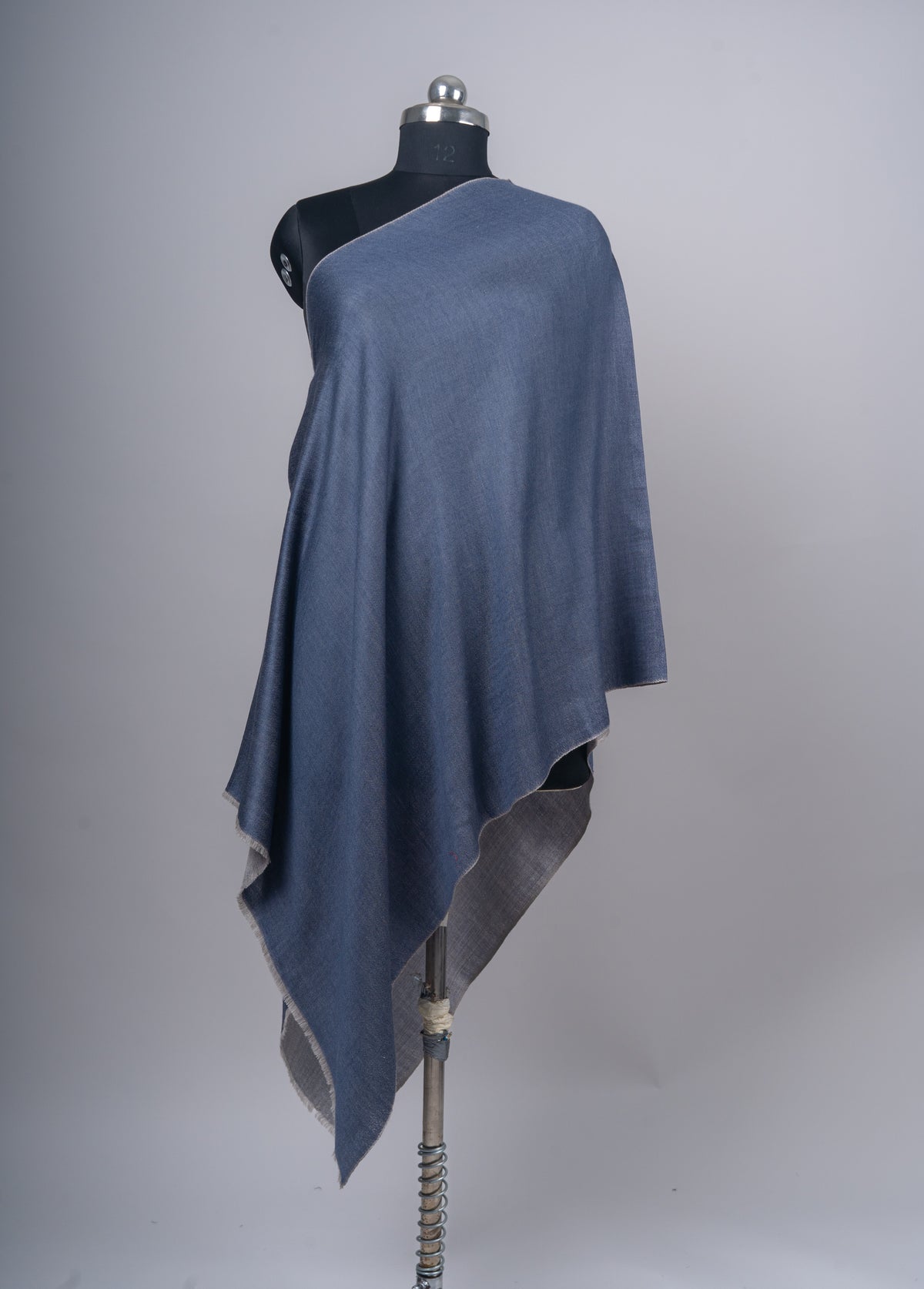 Full front view of the blue stole on a mannequin, with a long pointed fold and the grey reverse visible beneath.