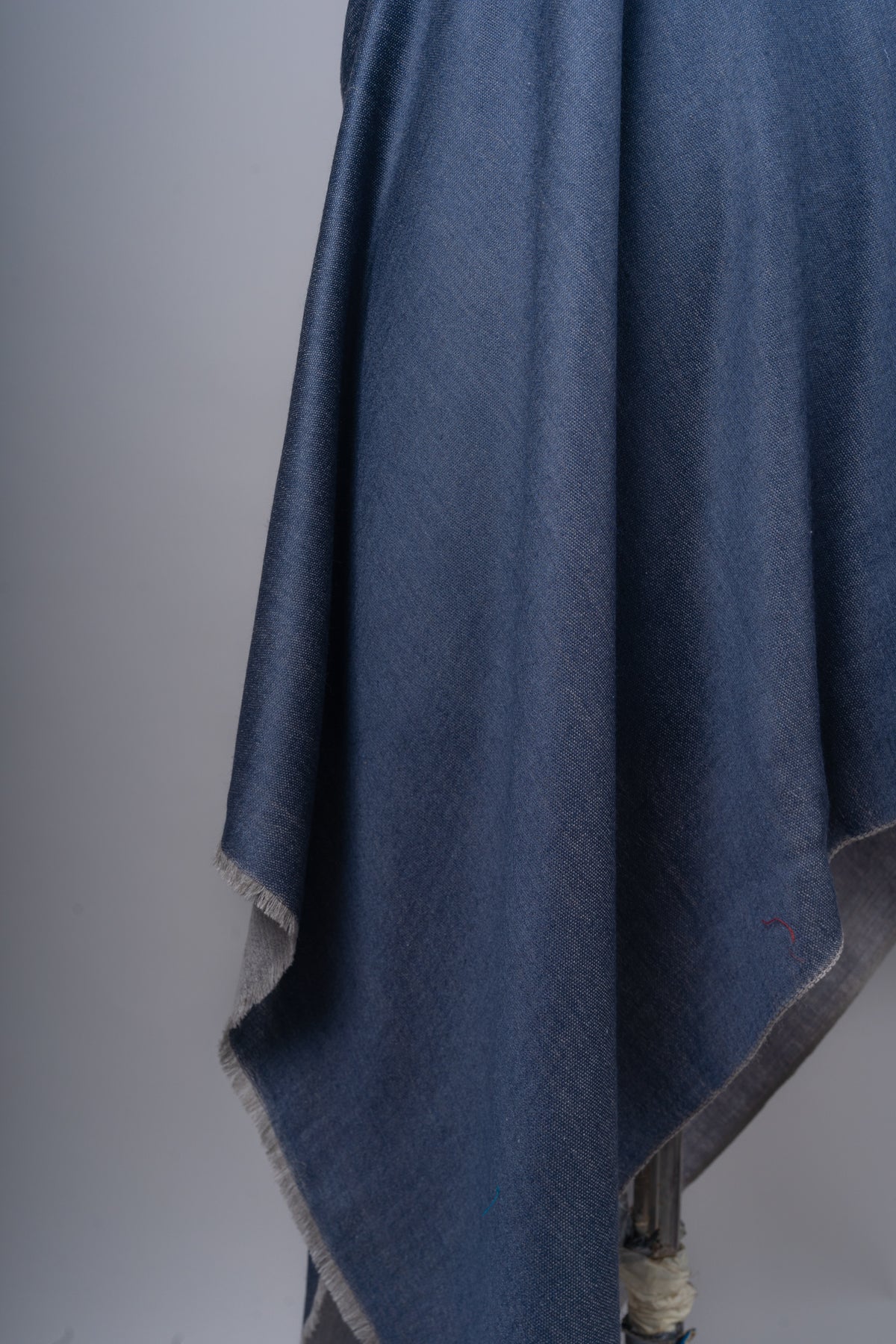 Close-up of hanging blue stole folds, with fine woven texture and a narrow grey reverse edge.