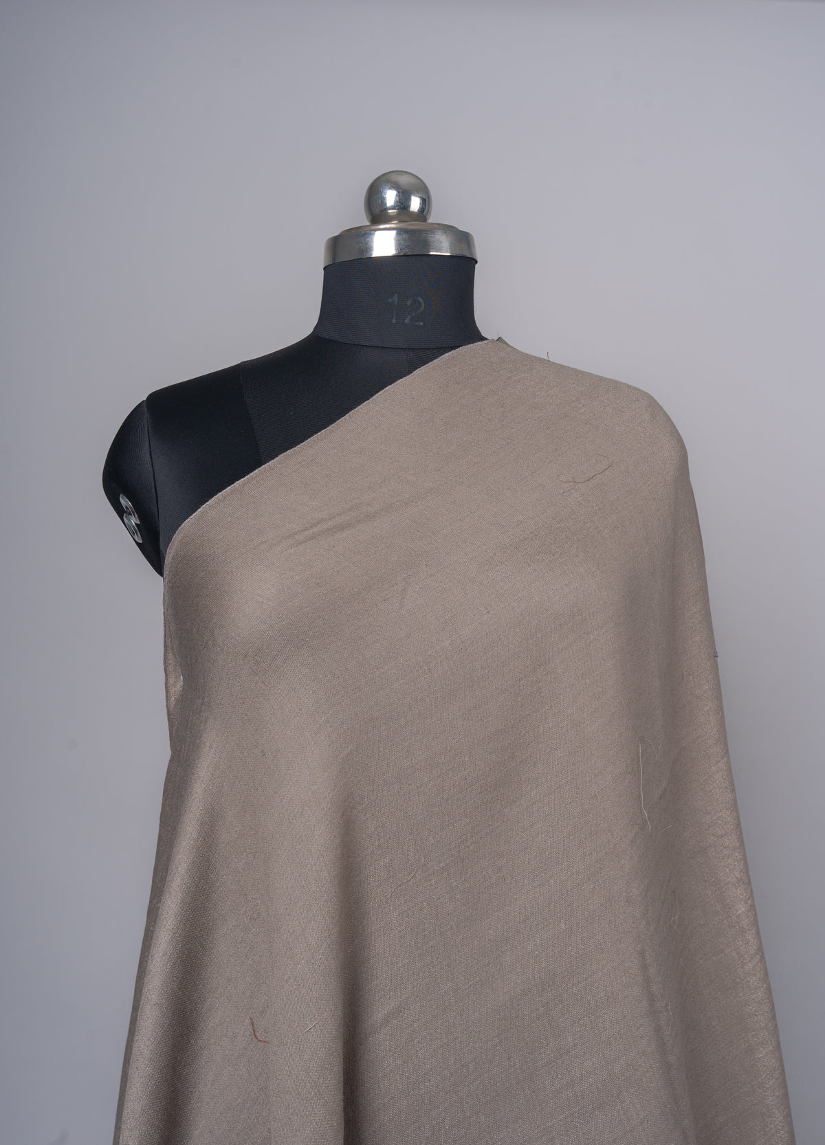 Close view of the taupe Merino wool stole across a mannequin’s chest, showing its plain woven texture