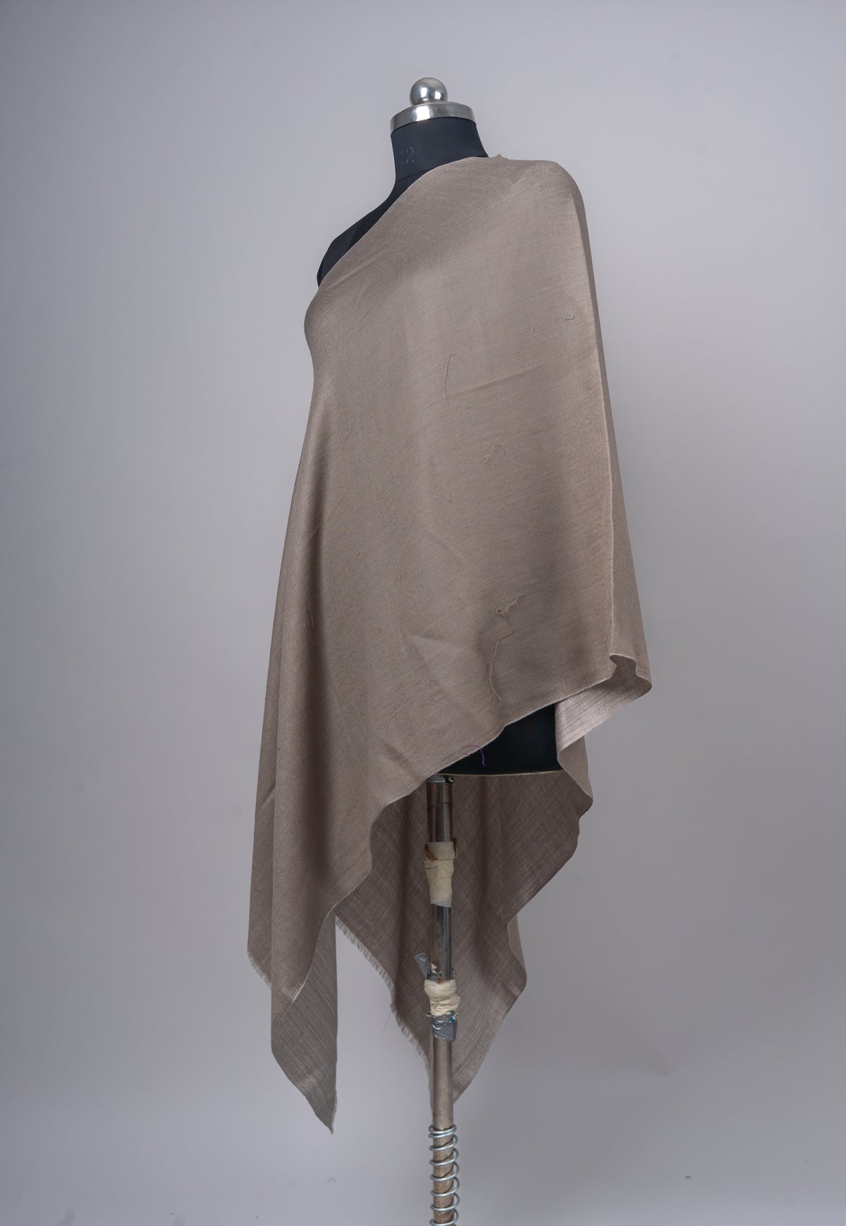 Angled view of the taupe Merino wool stole over one shoulder, with its lighter reverse visible in the hanging folds