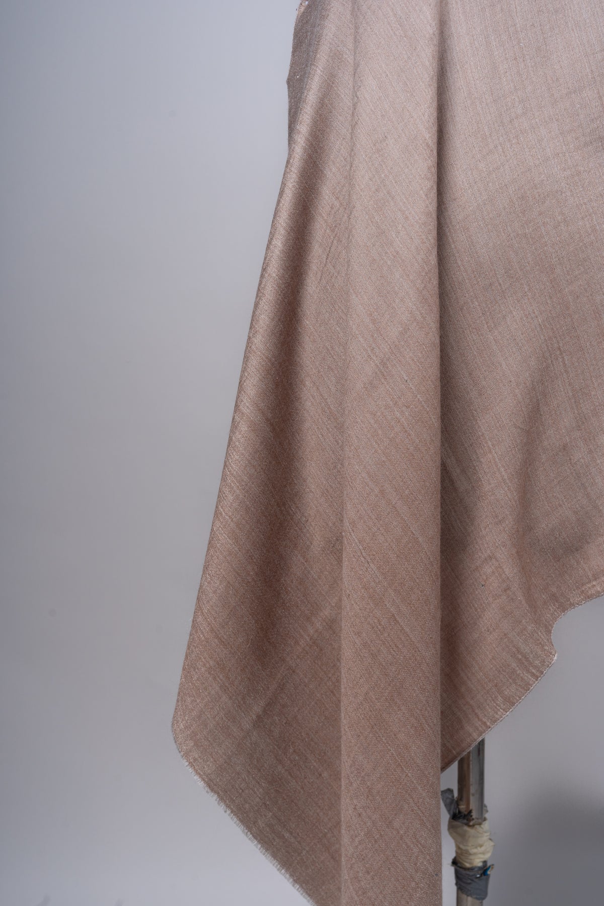 Detail of the hanging beige stole with soft folds and a short fine fringe along the edge.